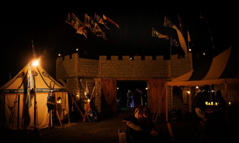 A castle at night, heralding flags raised, illuminated by lantern light